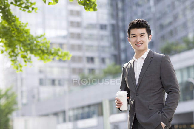 Uomo d'affari cinese in piedi sulla strada con tazza di caffè — Foto stock