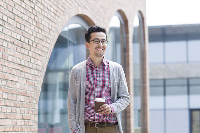 Chinese man holding cup of coffee in front of building — Stock Photo
