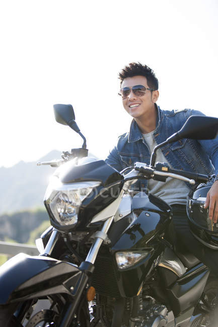 Hombre chino sentado en motocicleta en la carretera y sonriendo - foto de stock