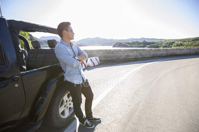 Homem chinês inclinado no carro e olhando para longe — Fotografia de Stock