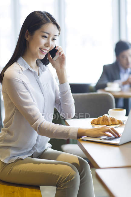 Китаянка разговаривает по телефону и использует ноутбук — стоковое фото