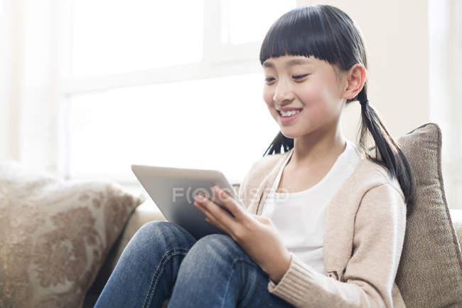 Chica china usando tableta digital en el sofá - foto de stock