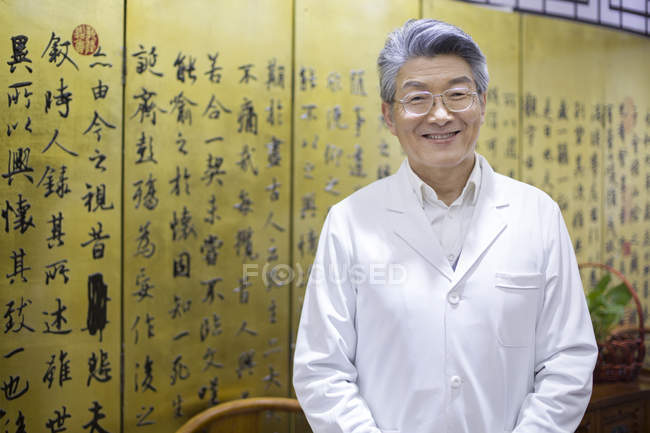 Старший китайський лікар, стоячи в клініку і дивлячись в камери — стокове фото