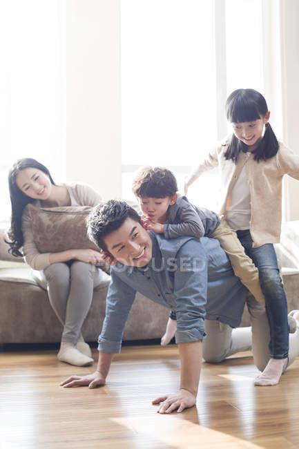 Chinesische Kinder spielen mit Vater auf dem Fußboden, während Mutter auf dem Sofa zuschaut — Stockfoto