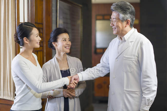 Chinese doctor shaking hands with patients in hospital hall — Stock Photo