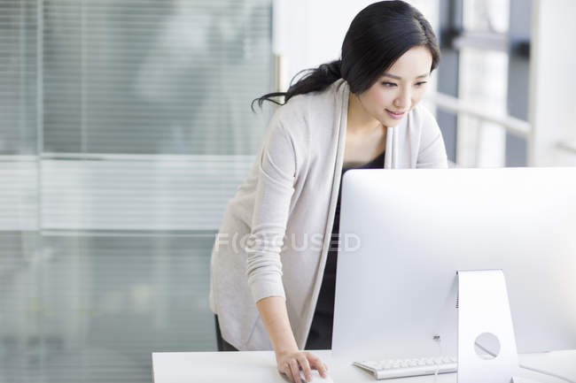 Mulher chinesa de pé e usando o computador no escritório — Fotografia de Stock