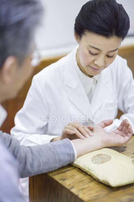 Female Chinese doctor taking pulse of senior patient — Stock Photo