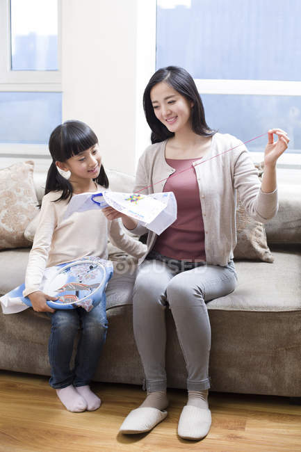 Chinese mother teaching daughter embroidery on sofa — Stock Photo