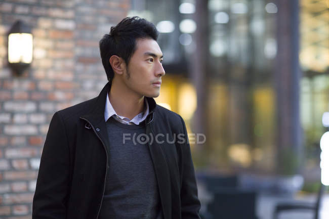 Pensive Chinese man standing on street and looking away — Casual Clothing,  street lights - Stock Photo | #184807760
