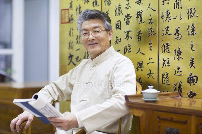 Senior chinesischer Mann in traditioneller Kleidung hält Buch — Stockfoto