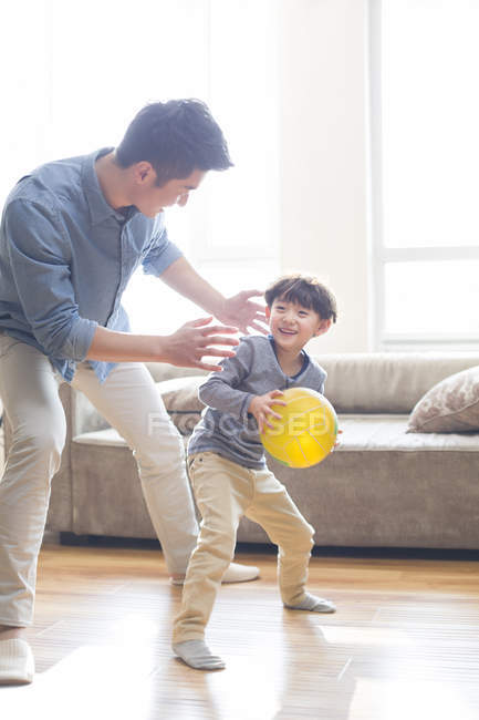Padre e figlio cinese che giocano con la palla gialla in salotto — Foto stock