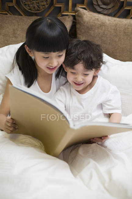 Chinese children reading book in bedroom — Stock Photo