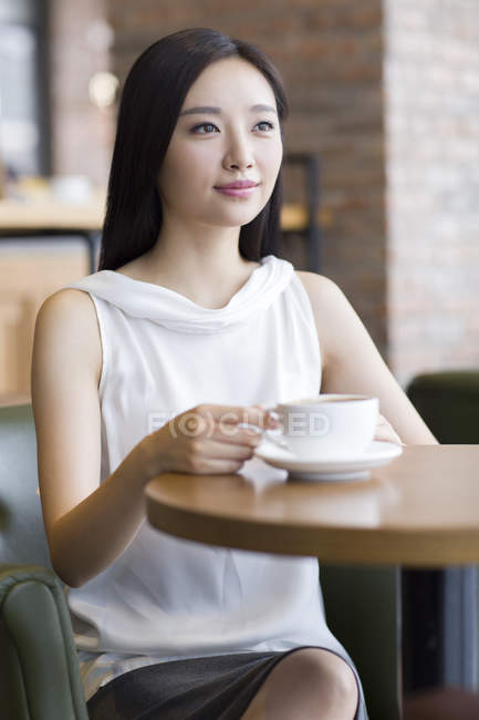 Chinesin sitzt mit Kaffee und schaut durchs Fenster — Stockfoto