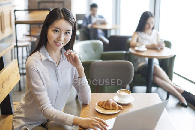 Chinese businesswoman sitting with laptop in cafe — Stock Photo
