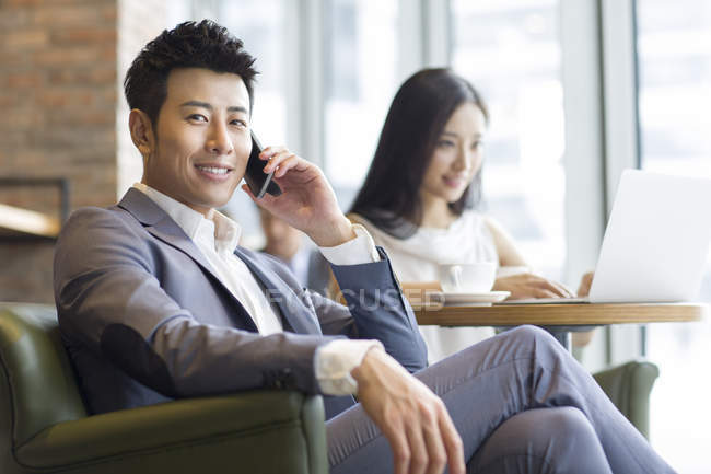 Китаєць розмовляємо по телефону з жінкою, сидячи у фоновому режимі з ноутбуком — стокове фото