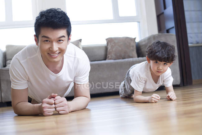 Père et fils chinois pratiquant la pose de planche à la maison — Photo de stock