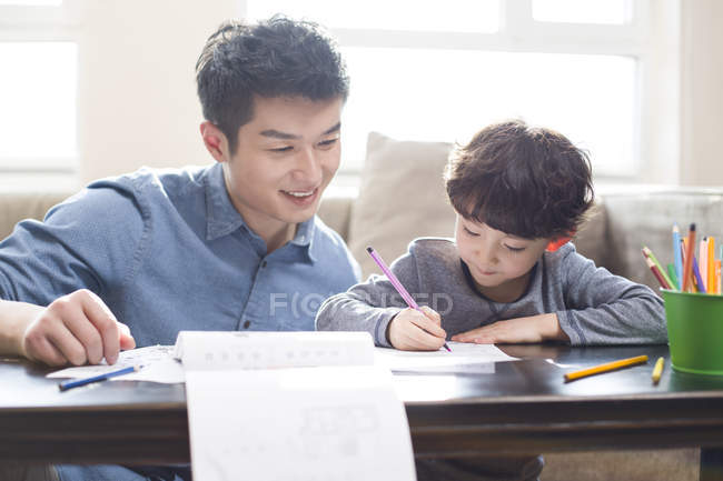 Chinese father smiling and helping son with homework — Stock Photo