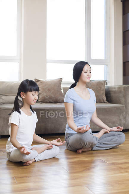 Madre e hija chinas meditando en casa - foto de stock