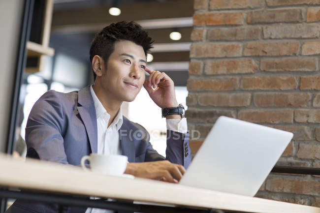 Uomo d'affari cinese seduto con computer portatile in caffè — Foto stock