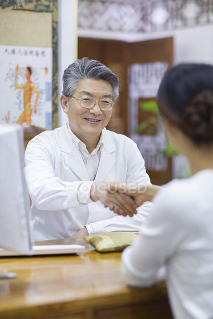 Китайский врач пожимает руку женщине в офисе — стоковое фото