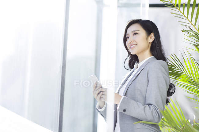 Chinese businesswoman holding smartphone in office building — Stock Photo