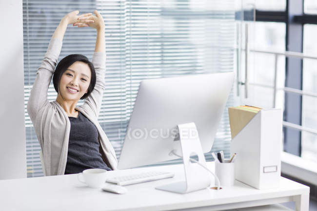 Mujer china estirándose y relajándose en la oficina - foto de stock