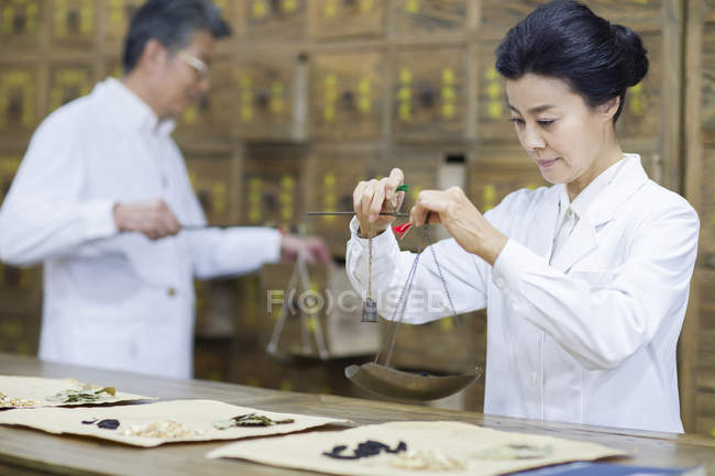 Chinese mature woman weighing herbs in pharmacy — Stock Photo