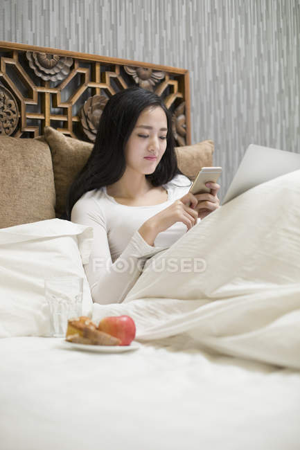 Mulher chinesa usando smartphone na cama — Fotografia de Stock