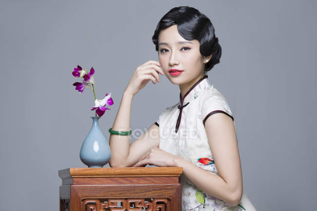 Chinese woman in traditional dress leaning on table with orchids — Stock Photo