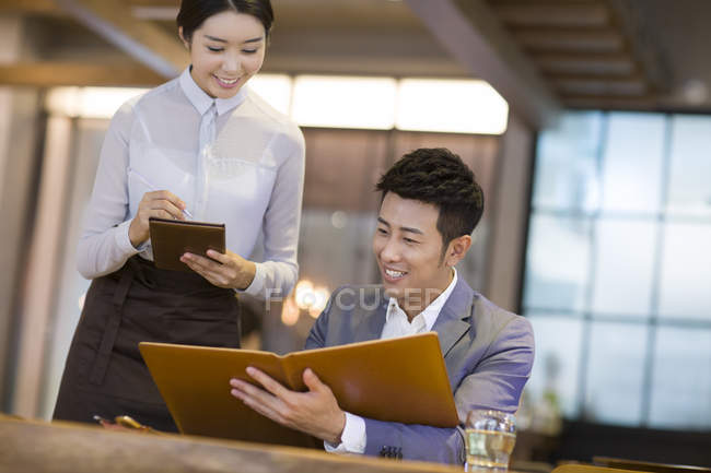 Chinese man ordering in restaurant with waitress — Stock Photo