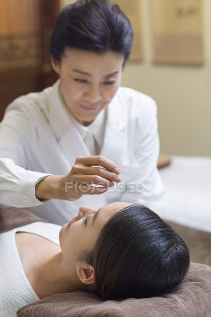 Mature woman performing acupuncture treatment on female face — Stock Photo