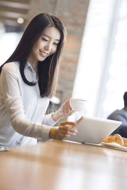 Chinesin benutzt digitales Tablet und hält Kaffee im Café — Stockfoto