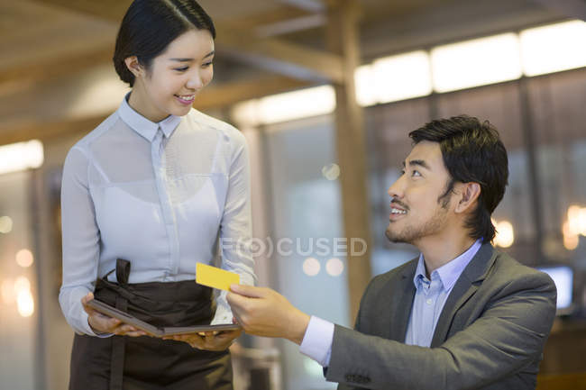 Hombre chino pagando con tarjeta de crédito en restaurante - foto de stock