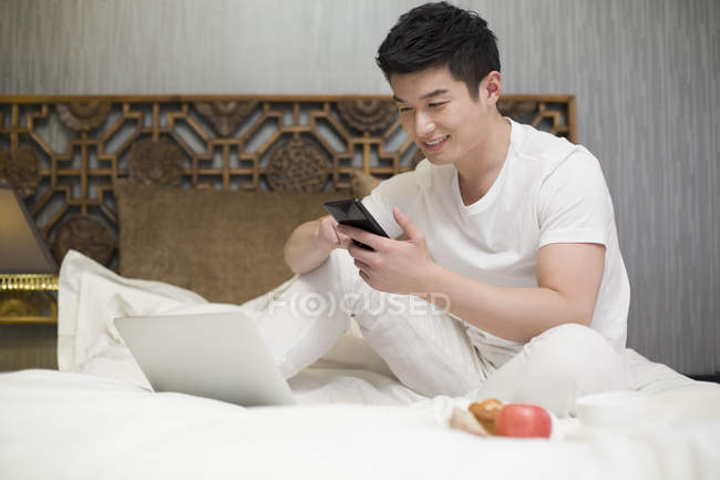 Hombre chino usando teléfono inteligente en la cama - foto de stock