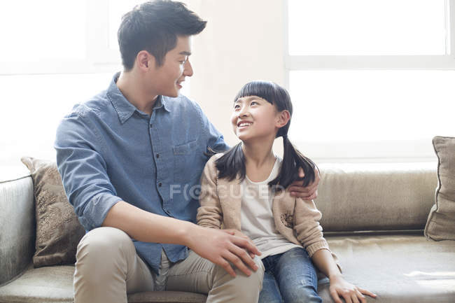 Padre e hija chinos sentados en un sofá - foto de stock