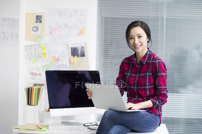 Diseñadora femenina china sentada en la oficina con portátil - foto de stock