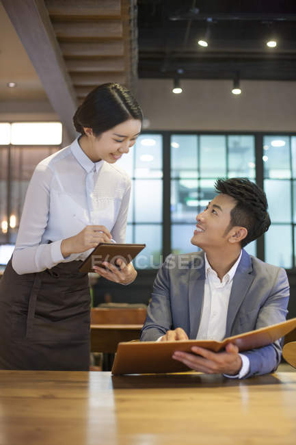 Hombre chino pidiendo en restaurante con camarera - foto de stock