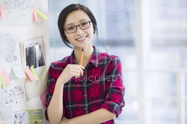 Chinese female designer standing at wall with sketches — Stock Photo
