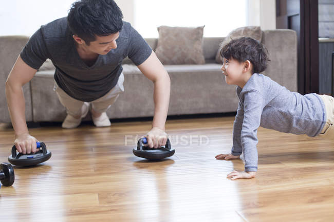 Padre e hijo chinos haciendo ejercicio en casa - foto de stock