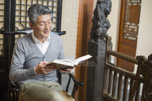 Homem chinês sênior sentado na cadeira e livro de leitura — Fotografia de Stock