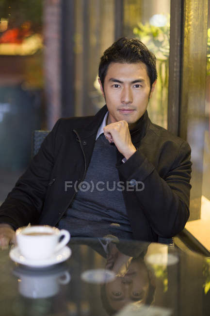 Hombre chino pensativo sentado en la cafetería de la calle - foto de stock