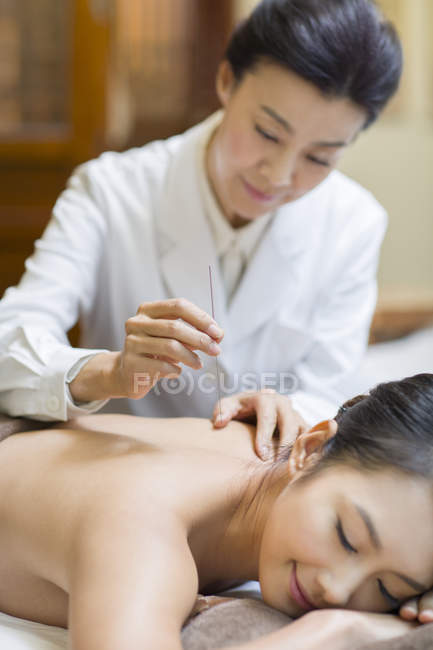 Mature woman performing acupuncture treatment on female patient — Stock Photo