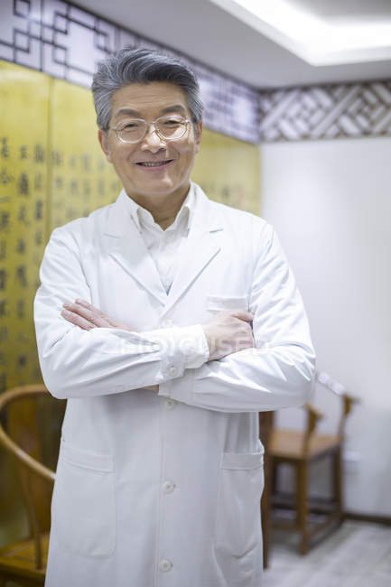 Médico chinês sênior de pé com os braços dobrados — Fotografia de Stock