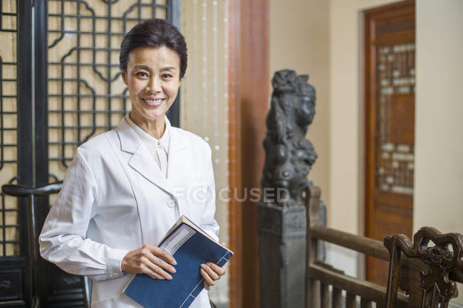 Doctora china sosteniendo libro y sonriendo - foto de stock