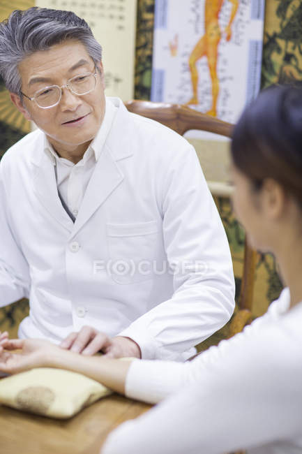 Médico chino senior tomando el pulso del paciente - foto de stock