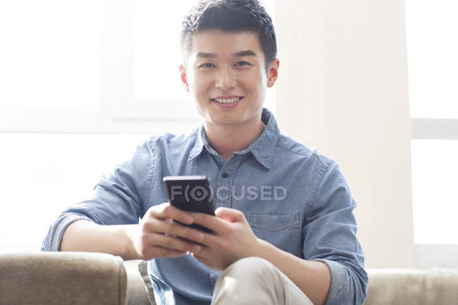 Hombre chino sosteniendo teléfono inteligente y mirando en la cámara - foto de stock