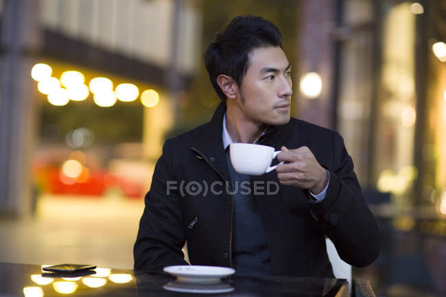 Chinese man drinking coffee at street cafe — Stock Photo