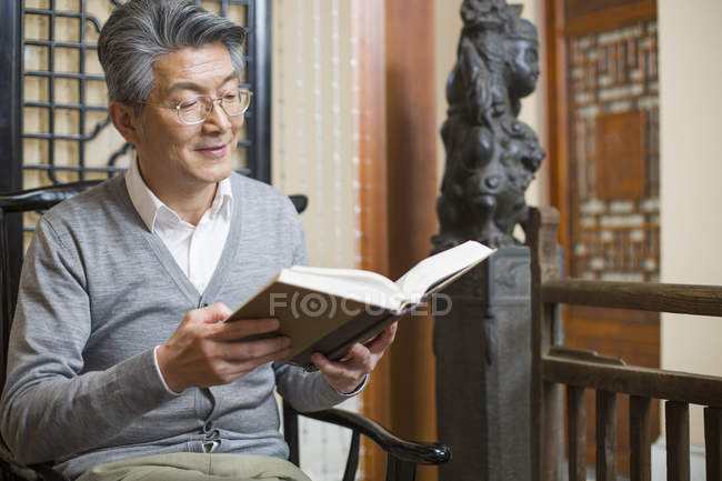 Старший китаец сидит в кресле и читает книгу — стоковое фото