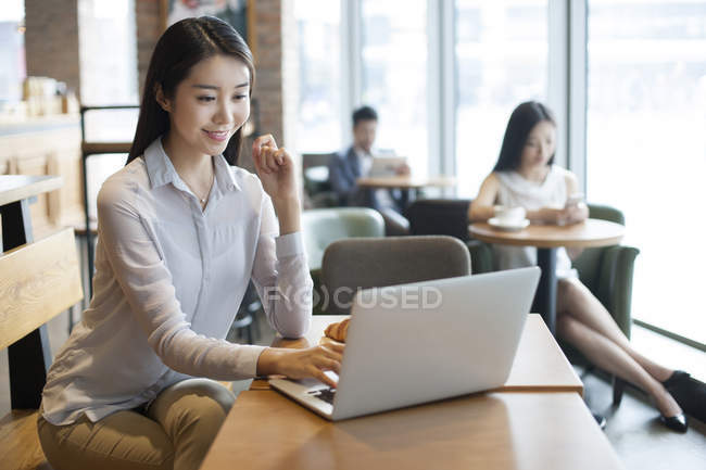 Mujer china usando el ordenador portátil en la cafetería - foto de stock