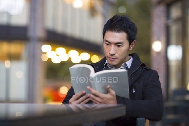 Chinese man reading book at street cafe — Stock Photo